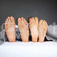 Its Sunday, put your laziest foot forward. a couples feet poking out from under the bed sheets.