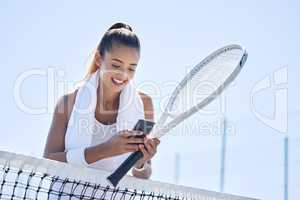 Active, fit and happy female tennis player browsing social media on her phone outdoors on the court. A young female athlete or sportswoman posting her sport training online or on the internet