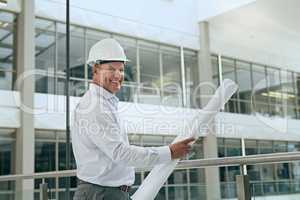 You can count on him to get the job done. Portrait of a cheerful professional male architect looking at the camera while holding blueprints inside a building.