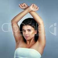 Confidence is beauty. Studio shot of a beautiful young woman with her arms raised and crossed against a blue background.