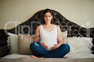 Preparing her spirit for his arrival. a pregnant woman meditating on her bed while cradling her belly.