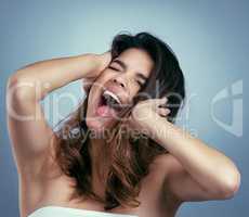 Such soft hair, it makes you scream. Studio shot of a beautiful young woman screaming against a blue background.