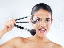 Makeup accentuates her natural beauty. Studio portrait of an attractive young woman holding makeup brushes against a gray background.