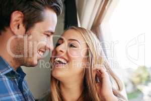 Laughter is a big part of their relationship. an affectionate young couple standing at a window in their home.