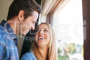 Love and laughter. an affectionate young couple standing at a window in their home.