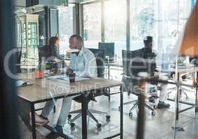 Business, office and work with a man sitting at his desk in a glass building and working with colleagues in the background. A busy corporate company with an employee and worker at a table for his job