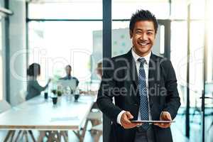 The ease and efficiency of this device is amazing. Portrait of a confident businessman using a digital tablet in an office.