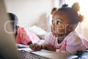 The internet is a wonderful place. an adorable little girl playing on a laptop next to her brother at home.