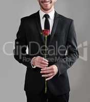 The perfect gentlemen attire. Studio shot of a well-dressed man holding a red rose against a gray background.