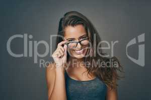 Like what you see. Studio shot of an attractive young woman peering over her glasses against a grey background.