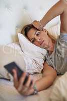 Oh no I didnt charge my phone last night. an attractive woman in bed looking at her phone in worry at home.