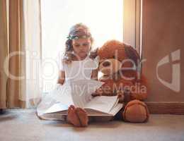 Words have ways of sparking a childs curiosity and imagination. an adorable little girl reading a book with her teddybear at home.