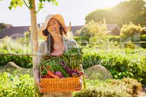 Grown by Mother Nature herself. Portrait of a young woman carrying a basket of freshly picked produce in a garden.