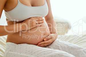 Youre loved little one. a pregnant woman touching her belly while sitting on her bed.