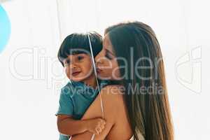 Time for cuddles with mommy. a young mother cuddling her little boy while he holds a balloon at home.