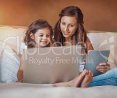 Exploring the world online together. a little girl using a laptop and her mother using a digital tablet at home.