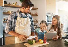 Knives are for grownups only, okay. two happy parents and their young daughter trying a new recipe in the kitchen together.