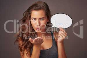 Sending love from the lips. Studio shot of an attractive young woman holding a blank speech bubble and blowing a kiss against a gray background.