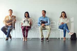 Their patience will be rewarded. a diverse group of people sitting in a row while waiting for a chance to interview.