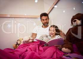 Shell be having lots of magical dreams tonight. a father reading a book with his little daughter in bed at home.