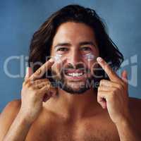 Keeping his skin hydrated and fresh. Studio portrait of a handsome young man applying moisturiser to his face against a blue background.