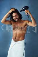 Use proper care to maintain great hair. Studio portrait of a handsome young man blowdrying his hair against a blue background.