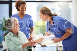 Lets get you admitted. a doctor holding medical records and shaking hands with a smiling senior woman sitting in a wheelchair.