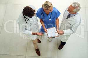 Brainstorming their way to a cure. High angle shot of a team of doctors brainstorming over a patients file in the hospital foyer.