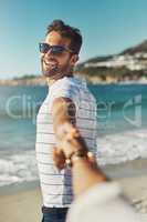 Follow me, to sun, sand and sea. a young man holding his girlfriends hand and leading the way at the beach.