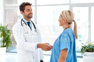 Working together for the good of the patient. two healthcare practitioners shaking hands in the hospital foyer.