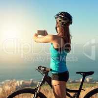 Mountain biking is an escape. a young woman taking a picture of the beautiful scenery while out mountain biking.