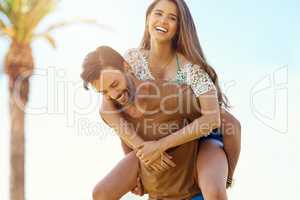 Carefree summer fun. a smiling young man giving his girlfriend a piggyback while enjoying a day together outside.