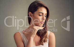 The face of contentment. Studio shot of an attractive young woman standing against a brown background.