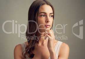 Quiet contemplation. Studio shot of an attractive young woman standing against a brown background.