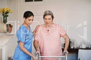 Slow and steady steps now...an attractive young female caregiver assisting a senior patient with a walker in a nursing home.