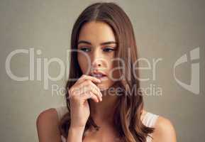 Contemplating quietly. Studio shot of an attractive young woman standing against a brown background.