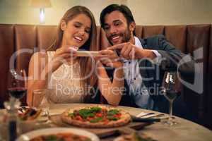 Delicious food to match the mood. a happy young couple taking a picture of their meal on a cellphone during a romantic dinner date at a restaurant.