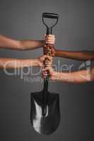 Lets dig in. Studio shot of unidentifiable hands holding on to a shovel against a gray background.