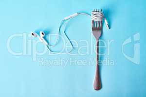 Music is the nourishment of life. Studio shot of earphones wrapped around a fork against a blue background.