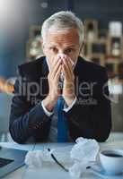 Maybe it will be over before I know. a frustrated businessman using a tissue to sneeze in while being seated in the office.