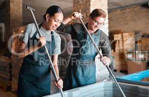 Cellar workers, making wine and mixing open tank with stirring, pressing and crushing tool for alcohol production. Happy staff and merchants in factory distillery, winery and manufacturing warehouse