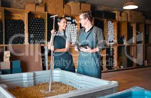 Winemaker partners crush grapes while researching the fermentation process on a digital tablet at winery. Young colleagues bonding and enjoying job, discussing the blend and flavor of last harvest