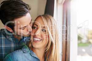 Fill everyday with love. an affectionate young couple standing at a window in their home.