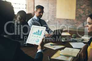 Statistics dont lie. Rearview shot of an unidentifiable businessman looking at graphs on his tablet during a meeting with his colleagues.