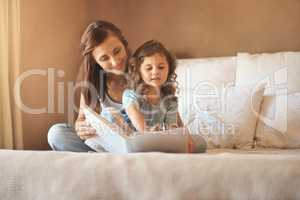 Please read it again mommy. a happy mother and daughter at home reading a storybook on the bed.