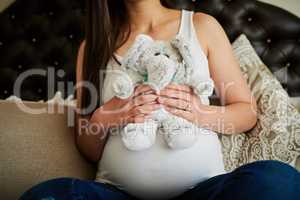 Playtime starts before her due date. an unidentifiable pregnant woman holding a stuffed toy while sitting on her bed at home.