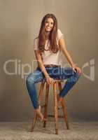 Kill them with kindness. Studio shot of a beautiful young woman sitting on a stool against a plain background.