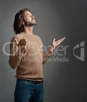 Praising His presence. Studio shot of a handsome young man praying against a gray background.