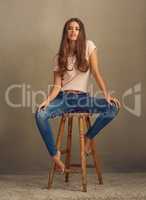 You have the power. Studio shot of a beautiful young woman sitting on a stool against a plain background.