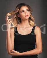 Beauty so enchanting. Studio shot of an attractive young woman twirling her hair against a dark background.